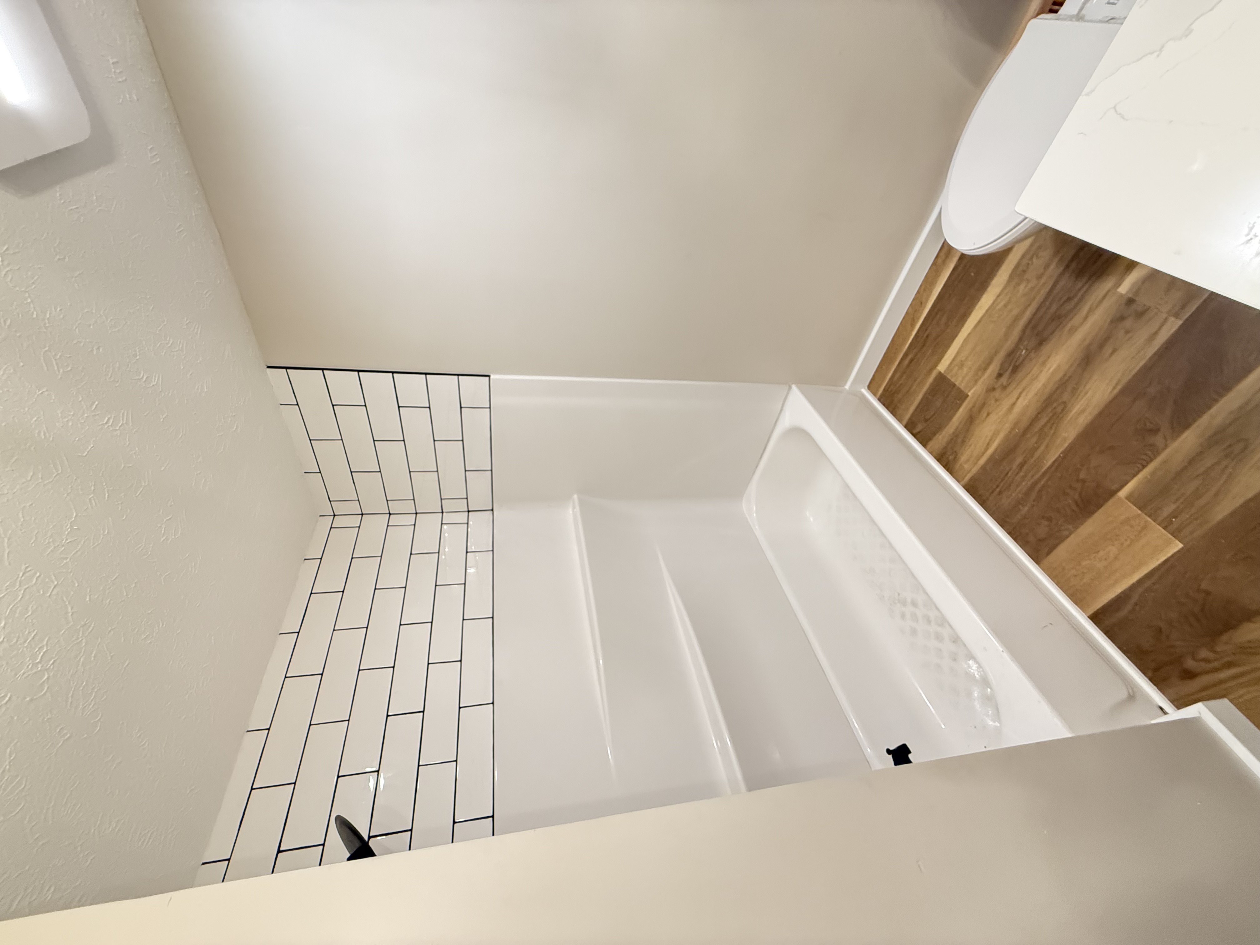 Subway tile tub surround with black grout and wood-look flooring
