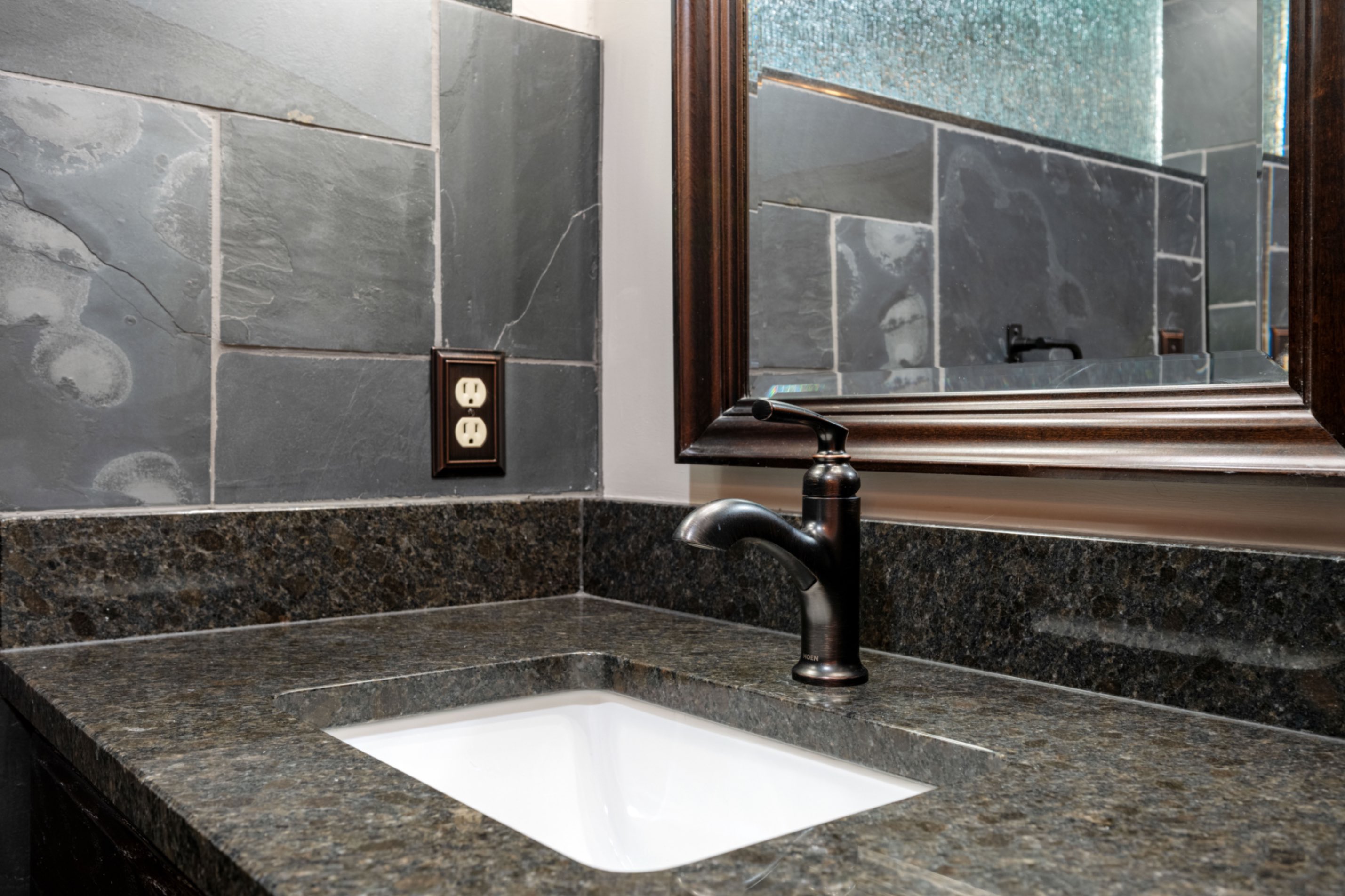 Granite vanity countertop with dark faucet and slate backsplash